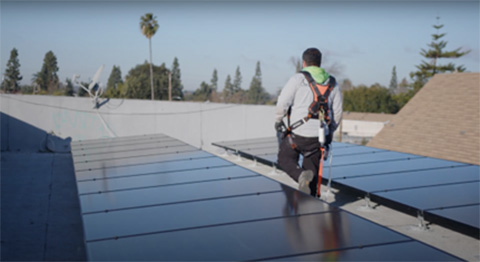 A solar installer walks between rooftop solar panels on a church.