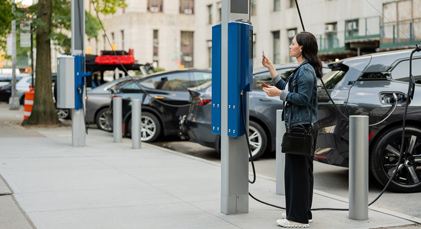 A woman standing at an electric vehicle charging station.