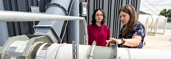 An mentor works with an intern on an outdoor piece of equipment.