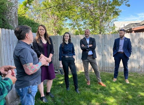 A group of people stand and talk in a yard on a sunny day.