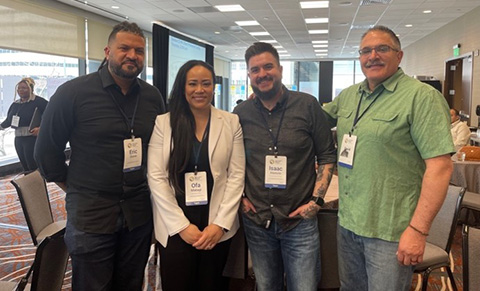 Four people stand smiling in a hotel conference room. 