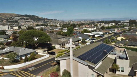 A photo looking down at a solar array on the roof of a large church in an urban setting.