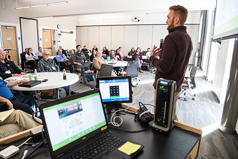 Presenter talks to a group of people in a conference room.