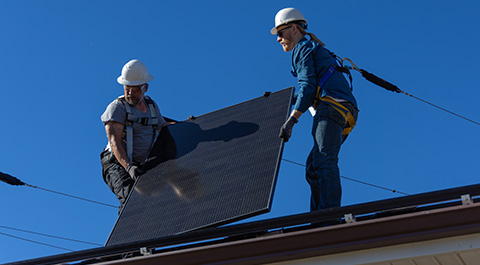 Two people install solar panels on a residential roof.