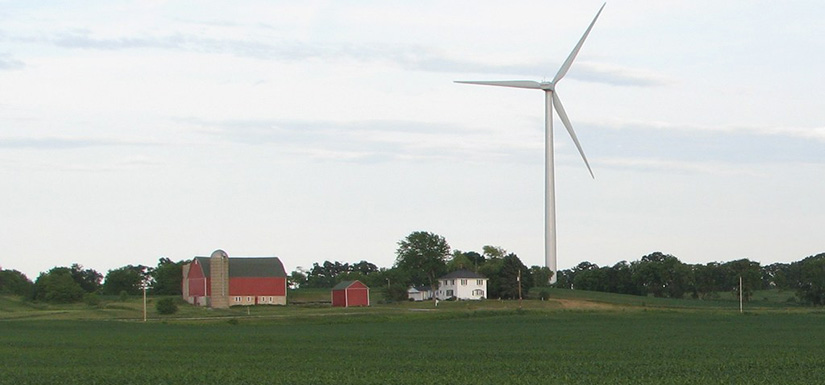 A farm with a barn and farmhouse in a field next to a wind turbine.