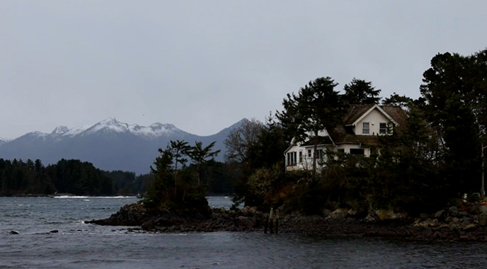 A house on a rocky coastline with mountains in the background.