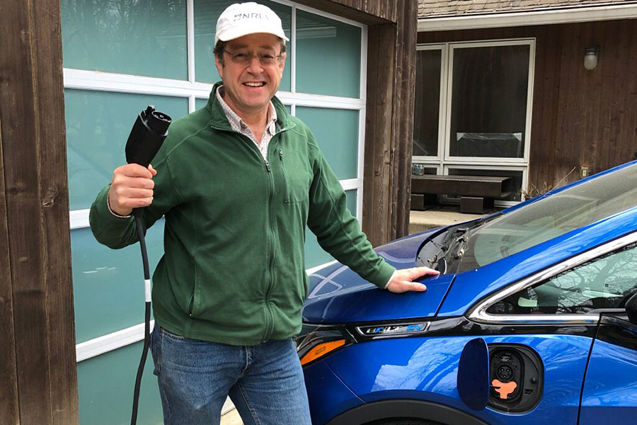 A person at home plugging in an EV to charge in a driveway.