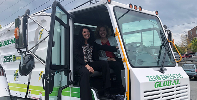 Two people sitting in the cab of an electric street sweeper.