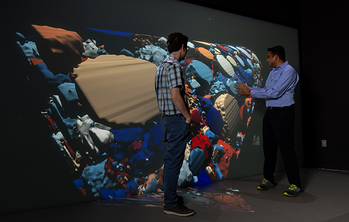 Two men looking at a colorful projection on the wall.