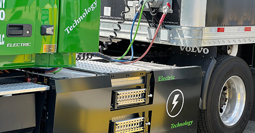 Detail photo of the electrical cables linking a green, 100% electric semitruck cab to its trailer.