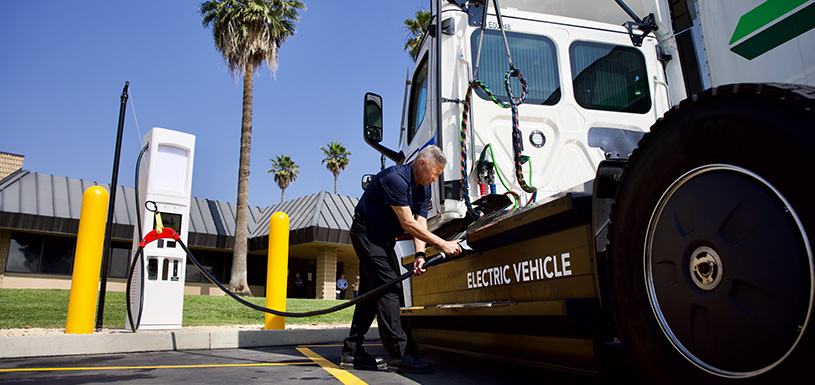 A man plugs a high-power charging cable into an electric semi-truck that reads Electric Vehicle.