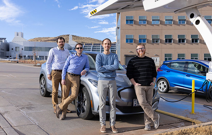 Four men stand in front of an electric vehicle being charged at NREL.