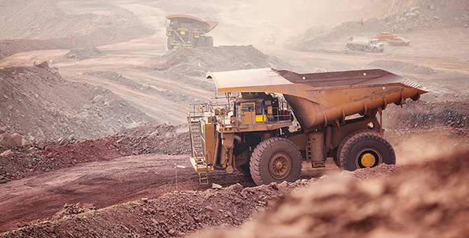 A large mining vehicle with a bed for carrying dirt on a dirt road surrounded by dirt and other mining vehicles.