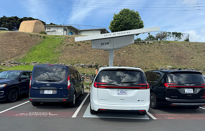 An electric vehicle plugged into a charger powered by a solar array mounted above the charging spot.