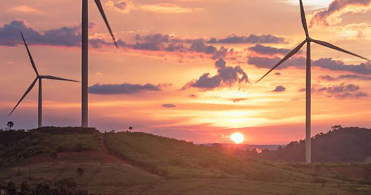 Three wind turbines in a grassy field while the sun is setting