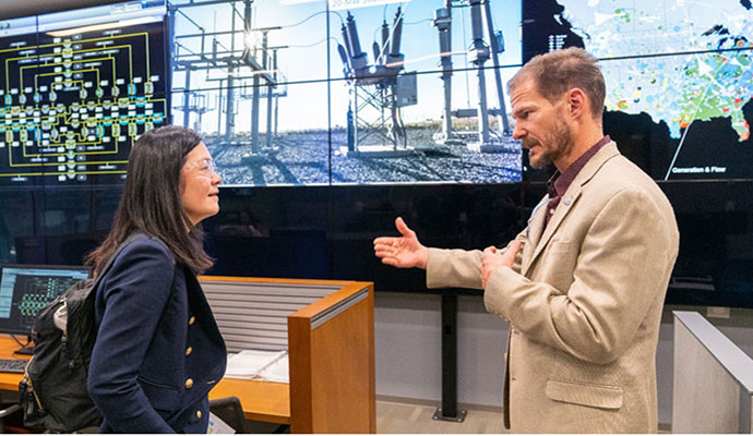 Two people talking in front of a large data display screen