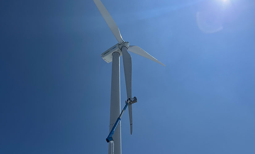 A worker in an extended aerial lift works on the blade of a wind turbine