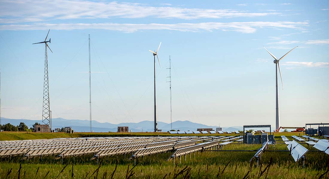 Three small wind turbines with a solar photovoltaic array in the foreground and mountains in the background.