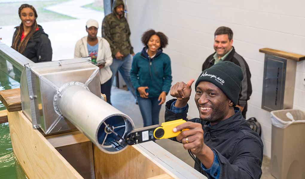 Person holds a thumbs up while checking out a technical devices while others stand around.