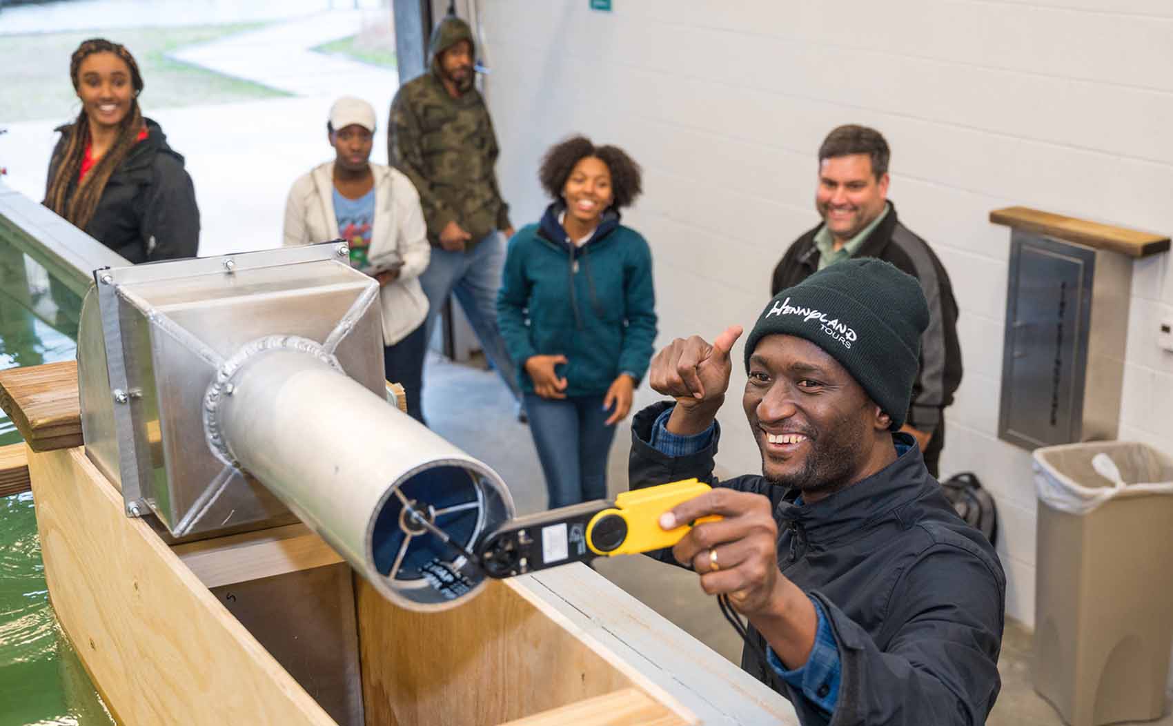 Person holds a thumbs up while checking out a technical devices while others stand around.