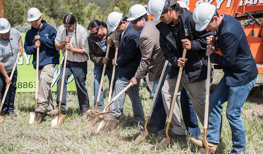 Group of people stand holding shovels to start digging in the ground.